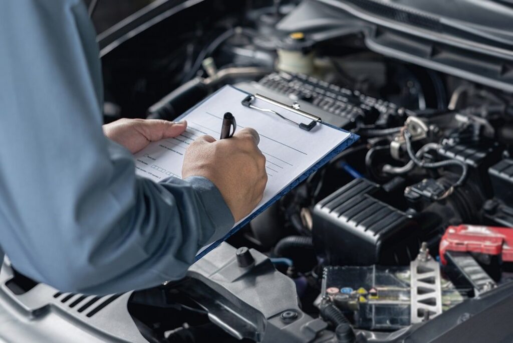 A mechanic is checking the engine of a car with a clipboard.